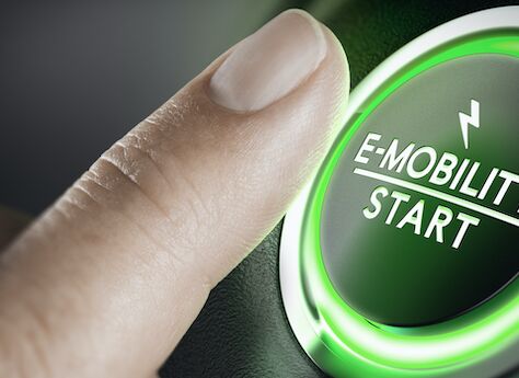 Das Bild zeigt eine Nahaufnahme eines Fingers, der einen grün beleuchteten Knopf mit der Aufschrift "E-MOBILITY START" und einem Blitzsymbol darüber drückt.