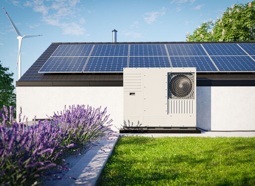Auf dem Bild ist ein modernes Wohnhaus mit Solarmodulen auf dem Dach und einer Wärmepumpe an der Hauswand zu sehen. Lavendel und Rasen im Vordergrund sowie ein Windrad im Hintergrund stehen für nachhaltige und klimafreundliche Energieversorgung.