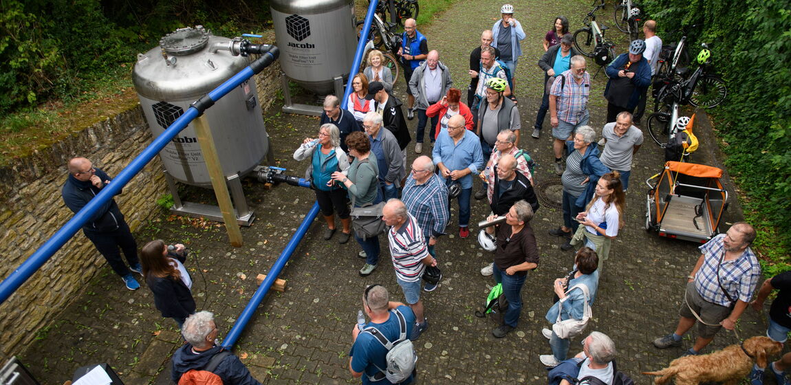 Das Bild zeigt zwei PFAS-Aktivkohlefilter in Heidesheim. Das Bild wurde beim Wasserradeln-Tag aufgenommen. Zu sehen sind außerdem etliche Zuhörer beim Vortrag von Lisa Gehrig zu den Filtern.