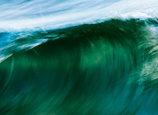 Das Bild zeigt eine große Ozeanwelle in verschiedenen Blau- und Grüntönen. Die Welle rollt sich über und erzeugt eine dynamische und kraftvolle Szene. Das Wasser scheint in Bewegung zu sein, und am Kamm der Welle bildet sich weißer Schaum.