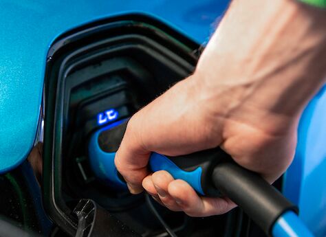 es wird ein blaues E-Auto betankt. Eine Hand hält das Ladekabel und steckt diese ins Auto.