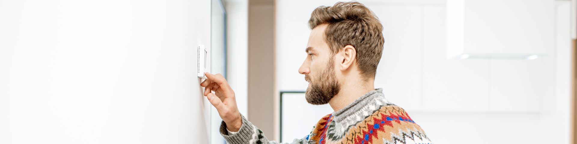 Das Bild zeigt eine Person, die einen Thermostat an einer Wand einstellt.
