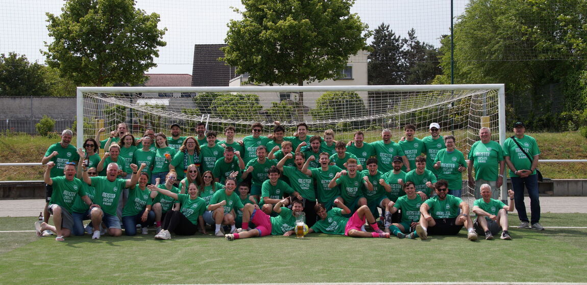 Zu sehen ist eine große Gruppe von Fußballspielern der Spielvereinigung Ingelheim. Die Spieler tragen alle ein grünes Trikot und haben sich auf dem Fußballplatz vor dem Tor platziert. Feudestrahlend lachen sie in die Kamera.