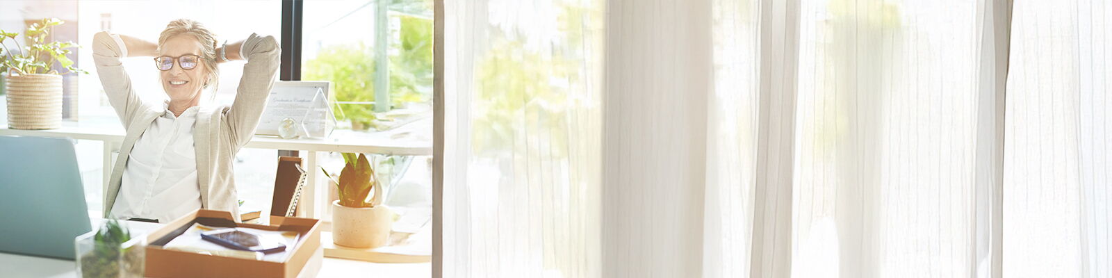 Zu sehen ist eine Frau mittleren Alters. Sie lächelt und lehnt sich entspannt in ihrem Schreibtischsessel zurück. Dabei blickt sie zufrieden auf ihren Laptop.