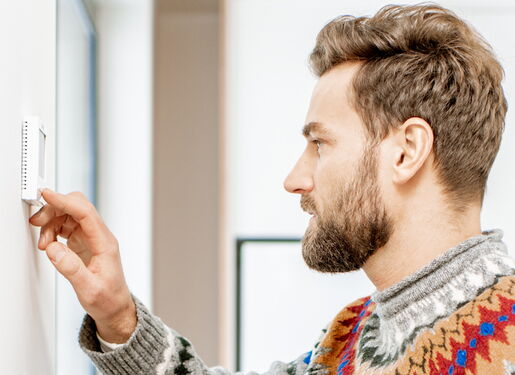Das Bild zeigt eine Person, die einen Thermostat an einer Wand einstellt.
