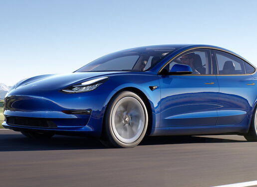 Das Bild zeigt ein blaues Elektroauto, den Tesla Model 3, das auf einer Straße fährt, mit Bergen im Hintergrund. Das Auto hat ein schlankes und modernes Design, mit einer glatten Karosserie und aerodynamischen Merkmalen.