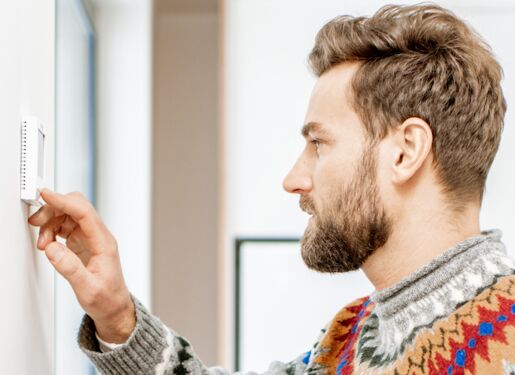 Das Bild zeigt eine Person, die einen Thermostat an einer Wand einstellt.