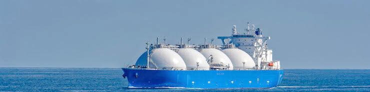 Ein Gasschiff mit 4 großen, weißen kugelförmigen Tanks auf dem Ozean. Der Himmel ist klar und blau, und das Wasser ist ruhig.