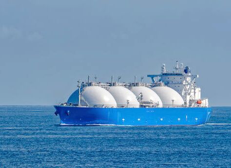 Ein Gasschiff mit 4 großen, weißen kugelförmigen Tanks auf dem Ozean. Der Himmel ist klar und blau, und das Wasser ist ruhig.