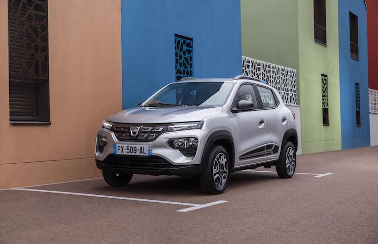 stehender silberfarbener Dacia Spring vor einer farbigen Häuerwand