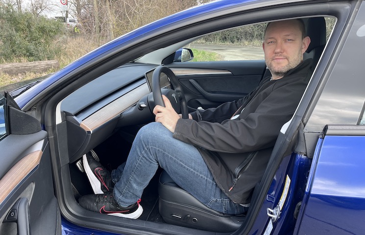 Frank Hilbrath sitzend in seinem E-Auto der Marke Tesla. Die Tür ist geöffnet.