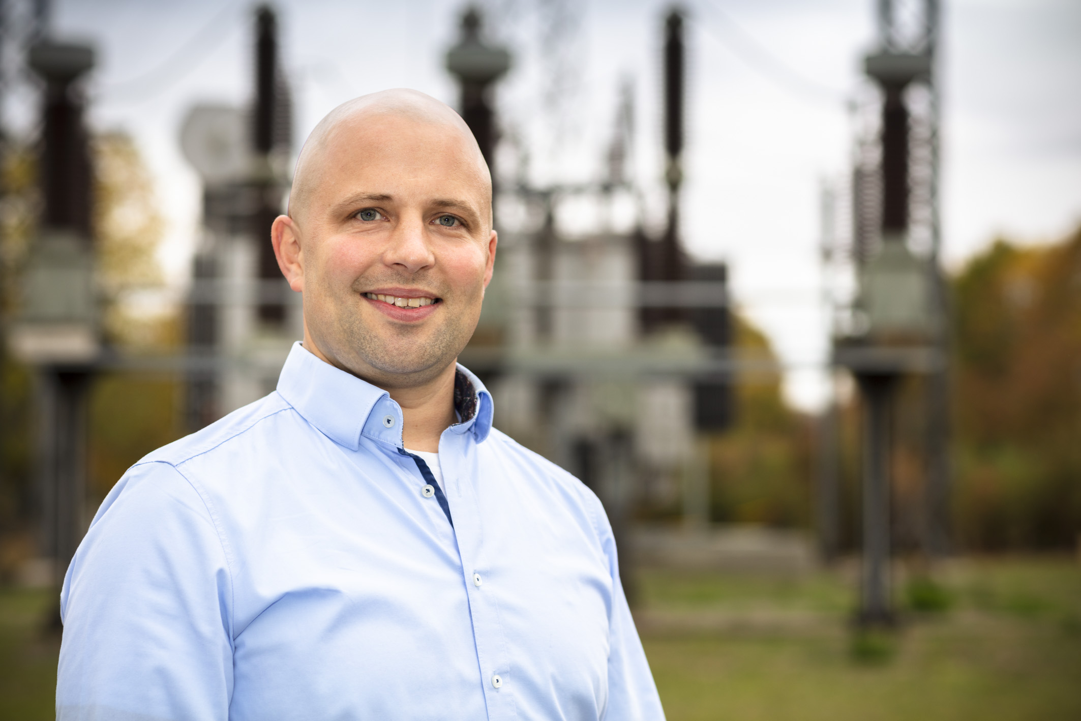 Christian Wendling trägt ein hellblaues Hemd und steht im Freien vor einer elektrischen Infrastruktur.