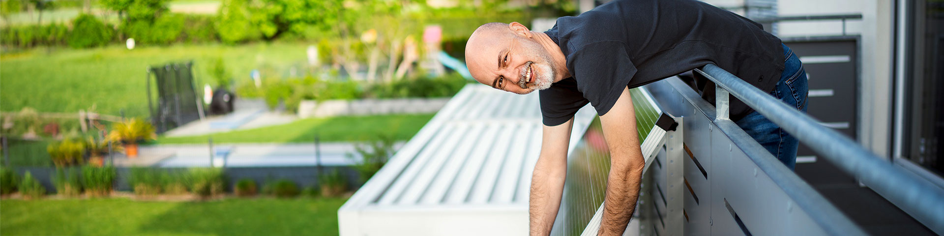 Das Bild zeigt eine Person, die sich über das Geländer eines Balkons lehnt und lächelt und an einem Solarpannel arbeitet.