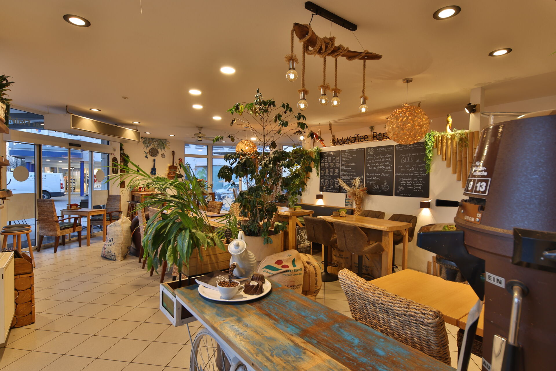Man sieht das Maja Kaffee in Ingelheim MItte von innen. Zu sehen sind Pflanzen, ein Holztisch, Stühle und beschriebene Tafeln.