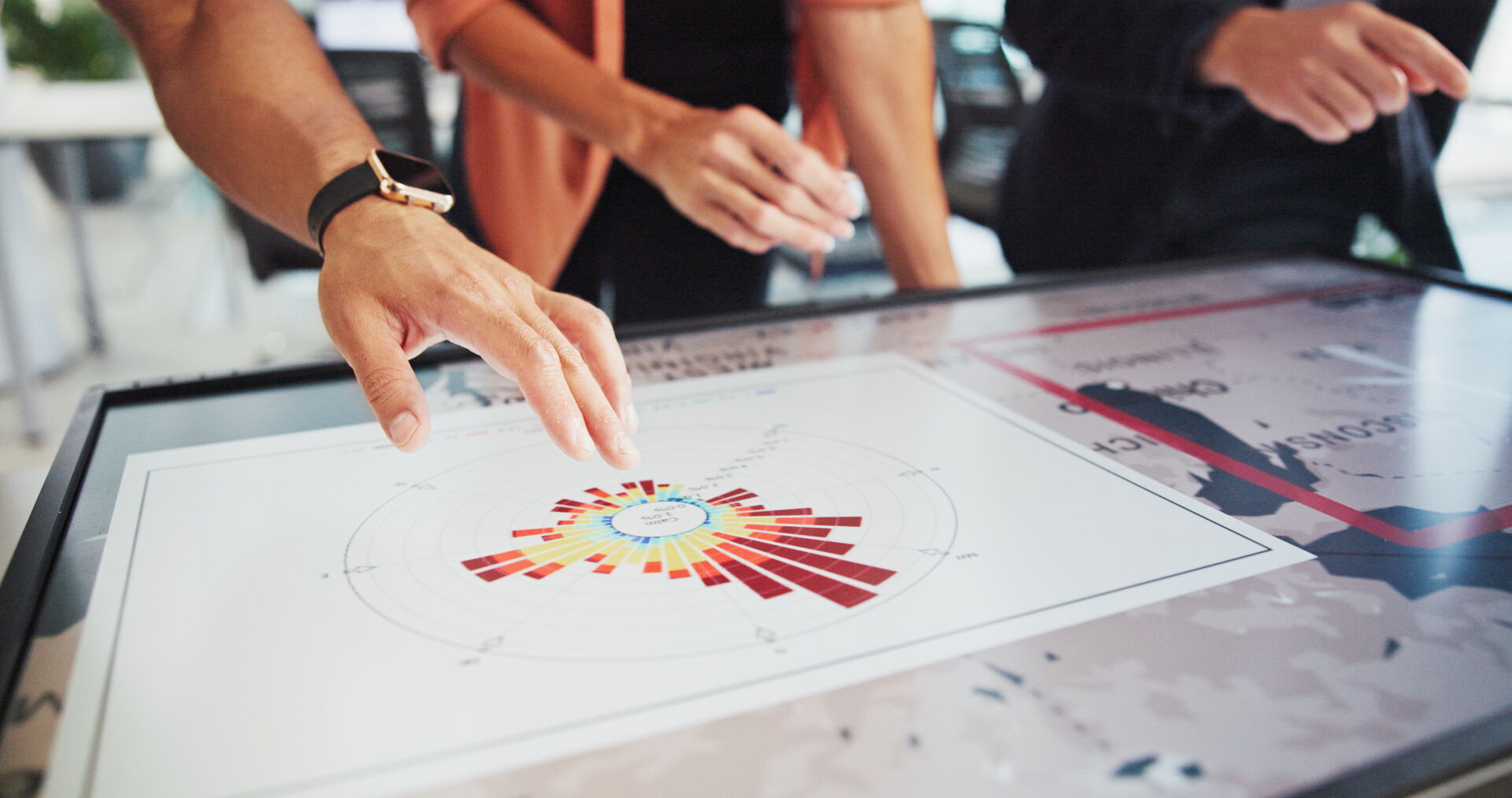 Das Bild zeigt eine Nahaufnahme zu einem Plan in Sachen Wärmeversorgung. Dahinter sind in der Unschärfe 3 Menschen zu sehen, die mit ihren Händen beziehungsweise Fingern auf den Plan deuten.