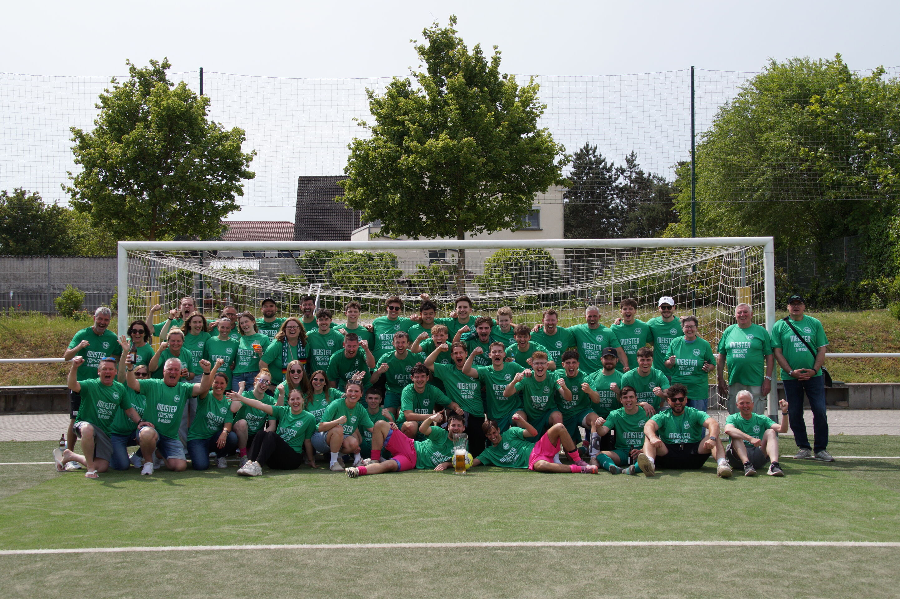 Zu sehen ist eine große Gruppe von Fußballspielern der Spielvereinigung Ingelheim. Die Spieler tragen alle ein grünes Trikot und haben sich auf dem Fußballplatz vor dem Tor platziert. Feudestrahlend lachen sie in die Kamera.