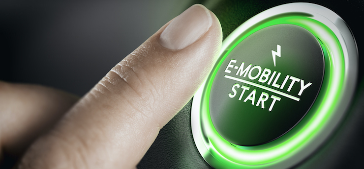 Das Bild zeigt eine Nahaufnahme eines Fingers, der einen grün beleuchteten Knopf mit der Aufschrift "E-MOBILITY START" und einem Blitzsymbol darüber drückt.