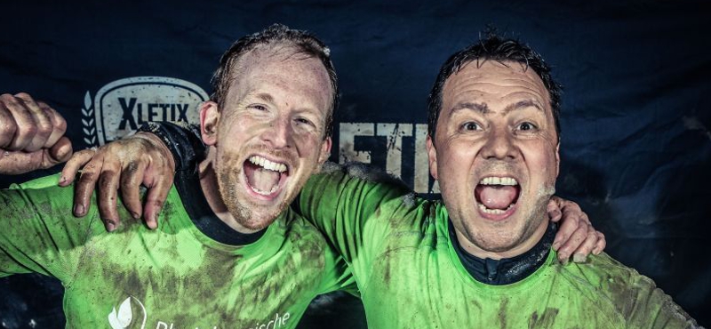 Jan Lubkowski und Viktor Hipp nach dem XLETIX Hindernislauf freudig umarmend. Beide sind mit Schlamm bedeckt.